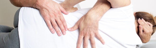 Zwei Hände führen eine chiropraktische Behandlung am Rücken einer liegenden Person durch.