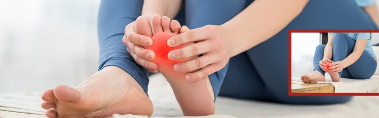 Person sitzt auf dem Boden und hält mit beiden Händen den Fußballen des rechten Fußes, der rot markiert ist.